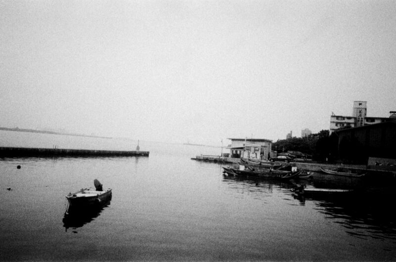 Tamsui: a small boat on flat water, mist over the river mouth. Black and white.