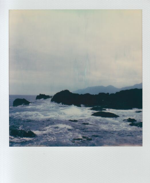polaroid: surf churning through black rocks, mountains dissolving in mist