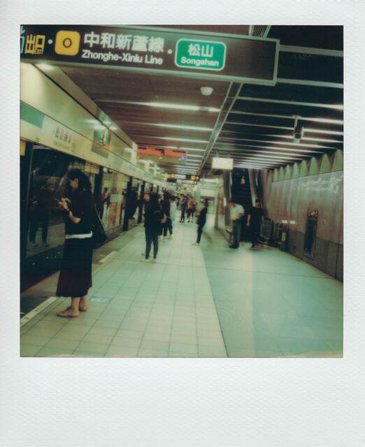 polaroid: mrt platform in green fluorescent light, a woman checking her phone