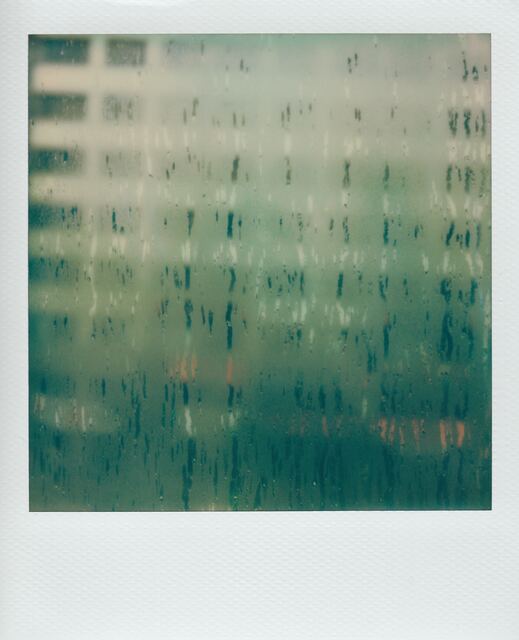 polaroid: condensation streaking a window, colored lights half-visible behind